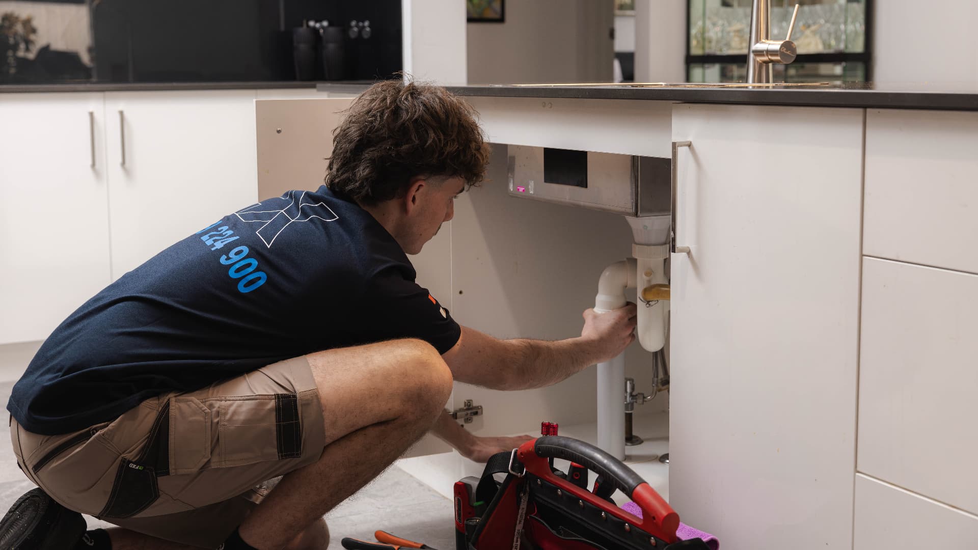 Fixara plumber repairing pipework under a kitchen sink in an Adelaide home